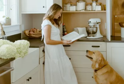 woman reads cookbook with dog in kitchen